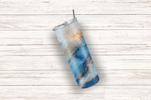 Thermobecher mit einem abstrakten Ozean-Design in Blau-, Türkis- und Goldtönen, liegend auf einem weißen Holzuntergrund, mit integriertem Trinkhalm und hochwertiger Verarbeitung.